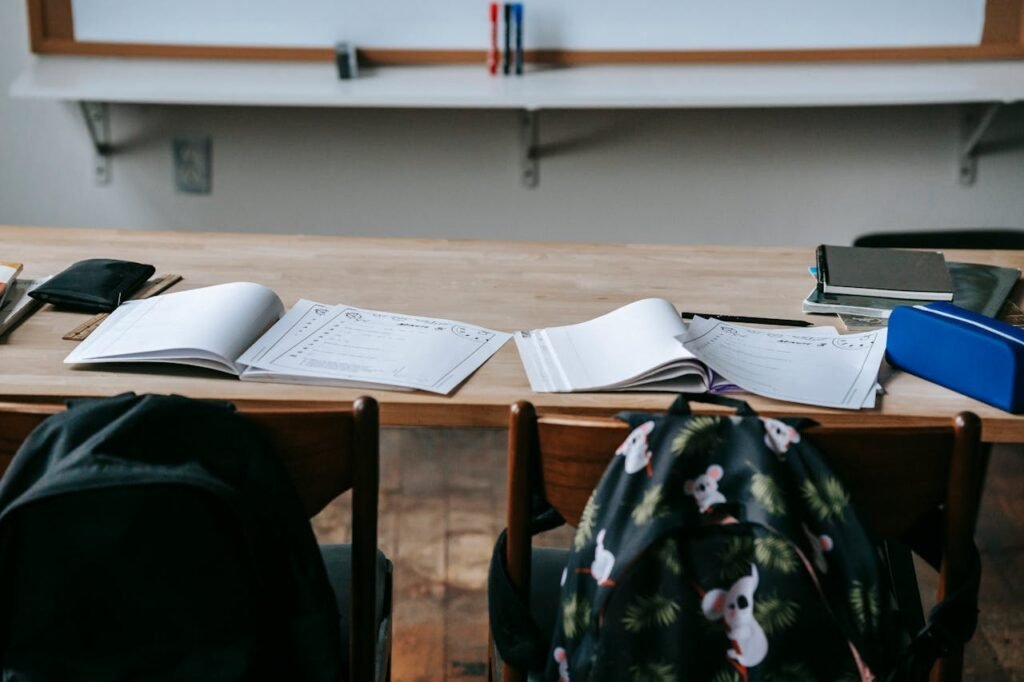 School desk with opened textbooks and stationery against whiteboard in modern light classroom